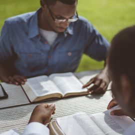 Two African-American male friends sitting at the table and reading the Bible at the table